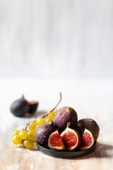 Composition with ripe fresh figs on grey plate and grapes. Healthy sweet dessert, no calories. Wooden light background, side light. Close up, copy space for your text