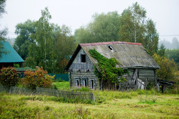 Fototapeta na wymiar old abandoned rickety old wooden house without windows with a partially missing fence in a distant village.