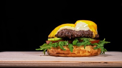 Craft burger is cooking on black background. Consist: sauce, arugula, tomato, red onion rings fries, cucumber, cheese, air bun and marble meat beef.