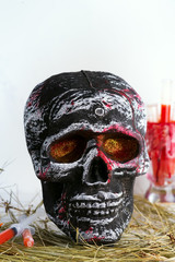 Skull with syringes with tomato juice in the hay as a decoration for Halloween party at home