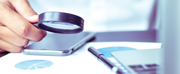 Businessmen use a magnifying glass to analyze the company's data and statistics from the chart.