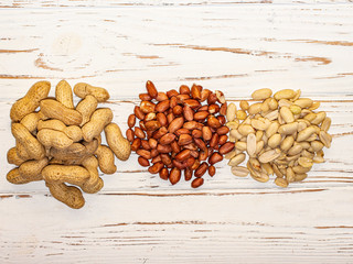 Three types of peanuts on a white wooden background.