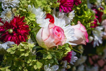 A bouquet of bright flowers, in the center of which are pink roses_