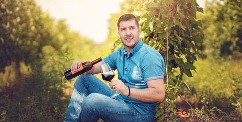 Young man pouring red wine in a glass in vineyard - Wine tasting in outdoor winery - Copy space