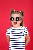 Cute little girl in sunglasses on red background