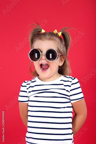 Cute little girl in sunglasses on red background
