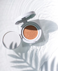 Korean foundation cushion with spf on the water surface under palm leaf shadow. Top view