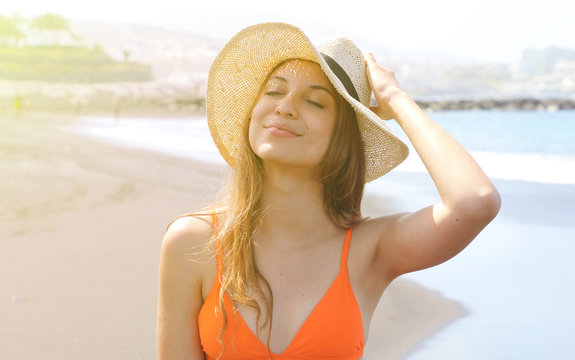 Young cheerful bikini woman with hat enjoying sun on tropical beach. Relaxing sunbathing holidays in Tenerife.