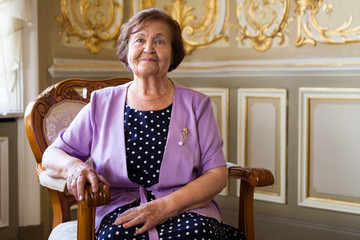 Senior Caucasian woman sitting in an armchair, smiling pension age female portrait indoors