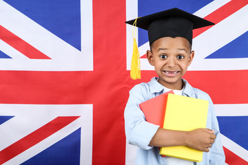 Cute boy in graduation cap with books on british flag background
