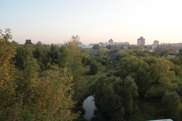 September forest and river landscape with background of blue evening sky and city buildings