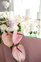 The wedding table setting for the newlyweds is decorated with fresh flowers of carnation, rose, anthurium and eucalyptus leaves. Silver candlesticks, white candles. Wedding floristry. Closeup details