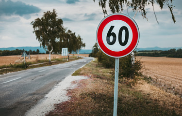 Illuminated photo of European speed limit road sign - 60 with road and field on background. Red...