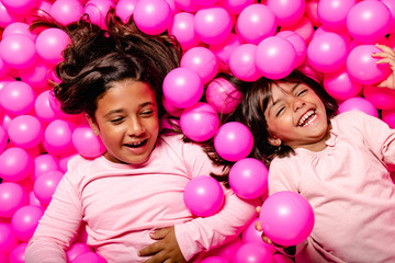 Fototapeta na wymiar two little girls smiling and playing at pink ball pool