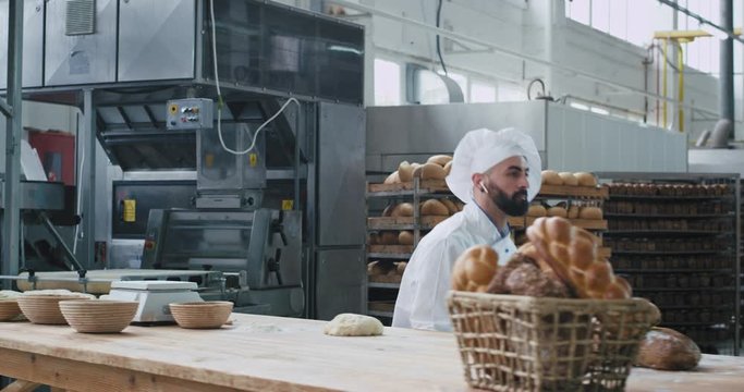 Good looking baker very funny at his work in a big bakery industry dancing and making funny faces while working with dough. slow motions