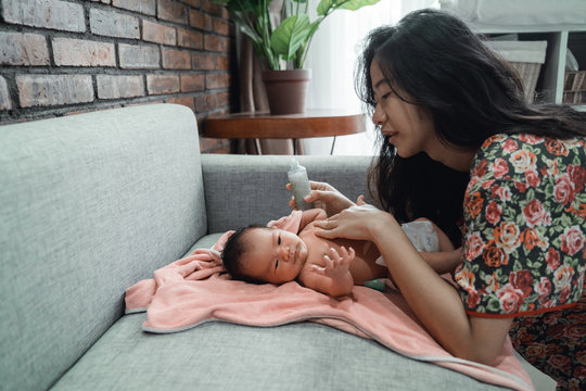 asian mother applying telon oil to her little daughter before bath at home