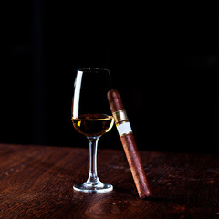 Whiskey glass with bourbon and fat cigar on the brown wooden table.Tall glass liquor and Cuban expensive hand rolled cigar,upper class life style