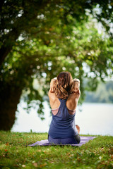 Obraz premium Rear view of fit Caucasian brunette sitting on mat in nature and practicing yoga.
