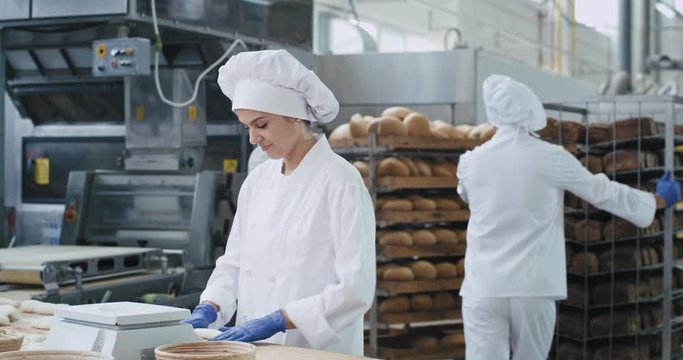 Attractive smiling beautiful bakers in a bakery kitchen industry portrait looking straight to the camera and enjoying the moment64. Working process at the bakery kitchen industry woman baker forming