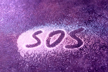SOS word hand written on white powder, distress signal.