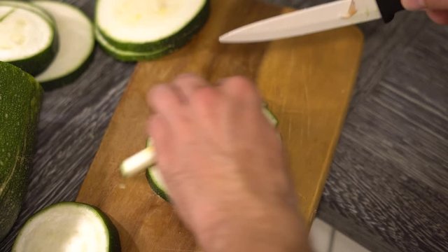 Zucchini mit einem Messer schneiden. Dunkelgr&uuml;ne Zucchini, die auf Holz-Schneidebrett in K&uuml;che