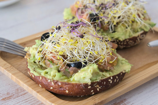 healthy brunch in a  wooden dish in table with veggie bagle with avocado, tomato, olives, outbreaks and olive oil. 