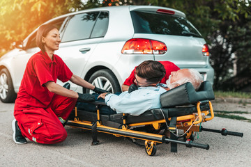 Emergency medical service at work. Paramedic is pulling stretcher with senior man with serious heart attack to the ambulance car. Help on the road. Drivers assistance concept..