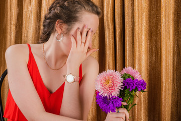 Intriguing girl with a bouquet of asters on a background of a golden curtain