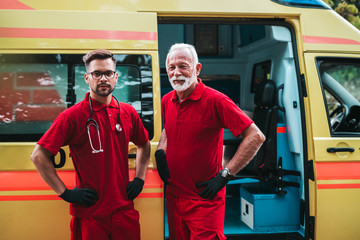 Emergency medical service male workers standing and posing in front of ambulance car.