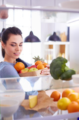 Smiling woman taking a fresh fruit out of the fridge, healthy food concept