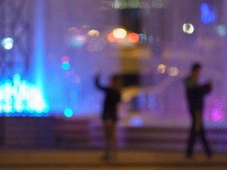 Blurred photography of the people near colorful fountain in the city park in night time. Romantic concepts of modern lifestyles.