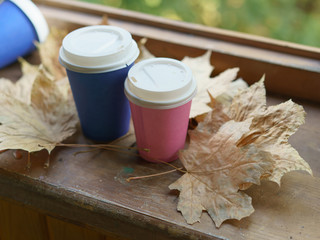 Photography of coffee paper cups standing and lying on the window with dried leaves. The end of the summer season and summer holidays. Concepts of relaxation and changes of lifestyle.