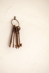 Bunch of old rusty keys hanging from a white wall.