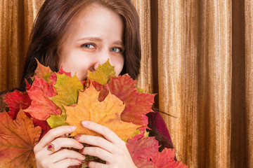 Smiling girl with a large bouquet of colorful autumn maple leaves on a background of a golden...