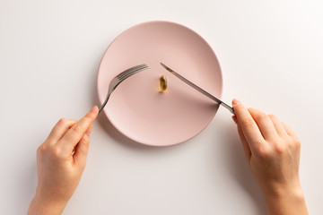 Female hands holding fork and knife. Plate with fish oil capsule. Flat lay.