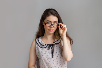 Emotions and people. A beautiful young brunette woman in a blouse, holding a hand on the arm of her glasses. Copy space