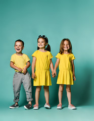 Fototapeta premium Studio portrait of children on a light background: full body shot of three children in bright clothes, two girls and one boy. Triplets, brother and sisters.