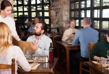 Fototapeta na wymiar Guests of the country restaurant discuss menu with waitress