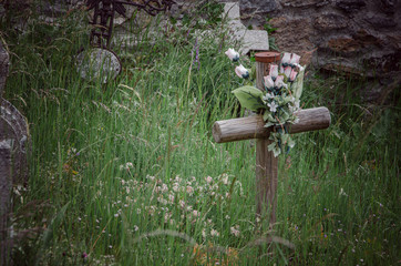 Wooden cross with plastic flowers among the grass