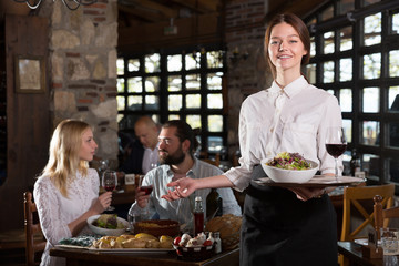 Fototapeta na wymiar Positive woman waiter demonstrating country restaurant to visitors