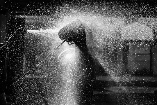 A black and white backlit  pictures of a horse being sprayed with water.