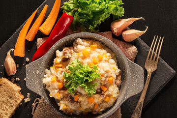 Frying pan with pilaf and fresh vegetables on a black wooden table.