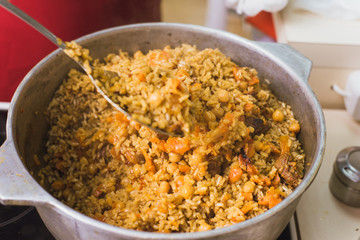 Cooking oriental pilaf in the kitchen in the cauldron. A woman prepares a dish of lamb, beef, rice, chickpeas, carrots