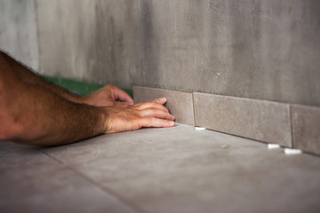 The construction master places the ceramic tiles on the floor.
