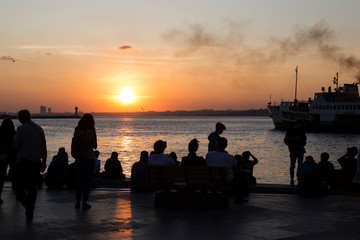 people sitting at the seaside and watching sunset and ferry.