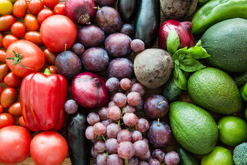 Different kinds of fruits and vegetables, top view. Bright violet grapes, plumps, colorful green avocado and basil leaves. 