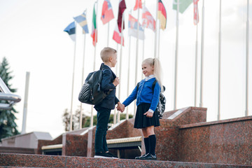 Little students go to school. Schoolchildren on background of flags of foreign countries.