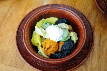 Colorful Russian pelmeni dumplings in a wooden bowl served with smetana sour cream
