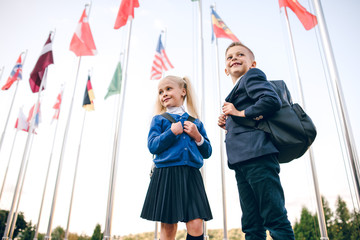 Little students go to school. Schoolchildren on background of flags of foreign countries.