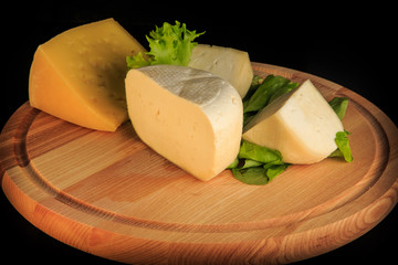 closeup assorted hard cheese on round wooden board